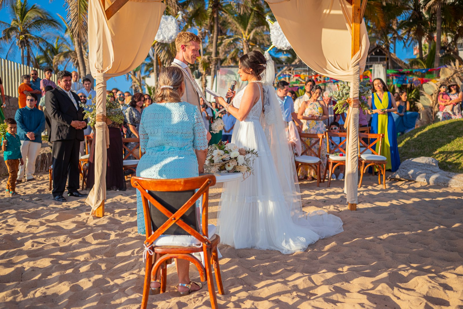 Wedding ceremony on a sandy beach with guests watching.
