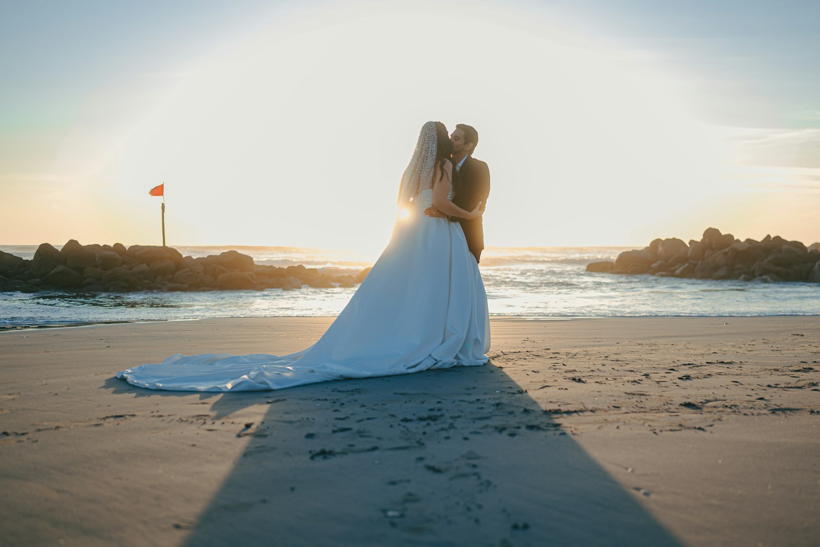 Bride and groom embracing on a sandy beach at sunset.